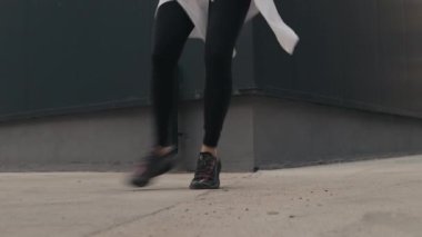 Şehirde hip hop yapan genç bir kadın belinde beyaz bir gömlek ile dans ediyor. Bir binanın yanındaki kaldırımda dans ediyor..