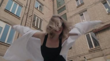 Bir apartmanın avlusunda gözlüklü, tasasız genç bir kadın dans ediyor. O neşe dolu ve kendini dans ve hareketlerle ifade ediyor..