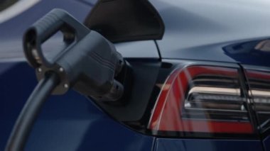 Modern şarj kablosuyla yüklü mavi bir elektrikli aracın yakın plan görüntüsü, sürdürülebilir ulaşıma doğru kaymayı vurguluyor.