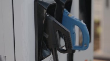 Siyah ve mavi şarj konnektörleri olan elektrikli araç şarj istasyonunun yakın görüntüsü. Modern elektrik taşıma altyapısını vurguluyor.