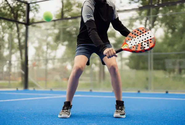 stock image A young athlete in action playing padel tennis on an outdoor blue court. Focus on the players legs and racket.