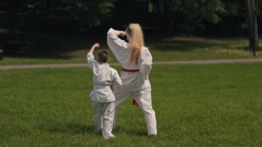 Kırmızı kuşaklı bir anne güneşli bir günde oğluna parkta karate öğretir. İkisi de beyaz karate üniforması giyiyor ve hareketlerini prova ediyorlar..