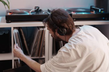 Kulaklık takan, plak koleksiyonuna göz atan, müzik çalan bir adam..
