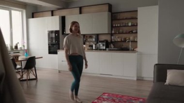 Bir kadın beyaz dolaplar ve ahşap döşeme ile modern bir mutfakta yürüyor, rahat ve çağdaş bir atmosfer yaratıyor..