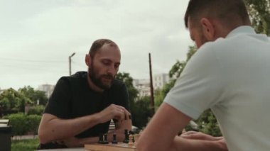 İki erkek arkadaş parkta satranç oynuyorlar. İkisi de hareketlerinde odaklanmış ve stratejik. Güzel bir gün ve park bir oyun için rahatlatıcı bir ortam..
