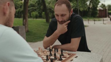 İki erkek arkadaş güneşli bir günde parkta satranç oynuyorlar. Bir sonraki hamlelerine konsantre oluyorlar..