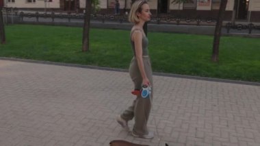 Genç bir kadın parkta Fransız Bulldog 'unu gezdiriyor. Onlar yaz havasının tadını çıkarıyorlar. Köpeğin tasması var. Bu klip mutluluk ve huzuru çağrıştırıyor..