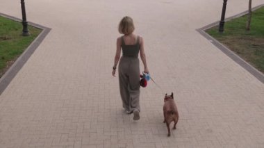 Fransız Bulldog 'unu fayanslarla döşenmiş bir parkta gezdiren bir kadın. Arkadan çekilen video rahatlatıcı ve huzurlu bir ortam sağlıyor..