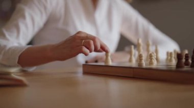Beyaz gömlekli bir iş kadını evdeki tahta satranç tahtasına stratejik bir hamle yapıyor..