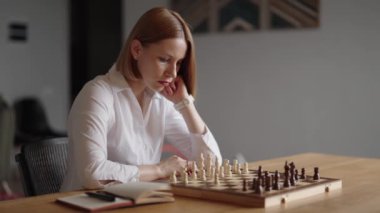 Beyaz gömlekli odaklanmış bir iş kadını satranç oyununda bir sonraki hamlesini planlıyor. Bu büyüleyici görüntüler strateji, karar verme ve rekabetçi ruh gibi kavramları somutlaştırır..