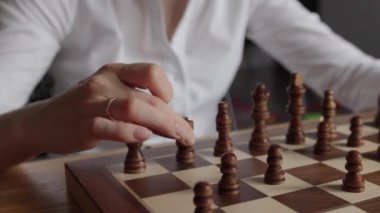 Beyaz gömlekli bir iş kadını klasik bir ahşap satranç tahtasına stratejik bir hamle yaparak strateji, iş ve karar verme temaları vurguluyor..