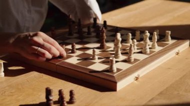 Beyaz gömlekli bir kadın ahşap bir masada oturur ve satranç oyununda hamle yapar. Videonun rahat ve stratejik bir havası var..