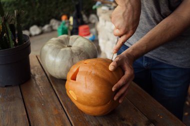 Bir insan, tahta bir masaya bıçakla balkabağı oyuyor ve Cadılar Bayramı kutlamalarına hazırlanıyor. Sahne, sonbaharın ve yaratıcı tatil hazırlığının özünü yakalıyor..