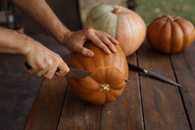 Kapalı çekimde, açık bir masa üzerine balkabağı oyan eller, sonbahar hazırlık ve yaratıcılığının özünü yakalıyor..