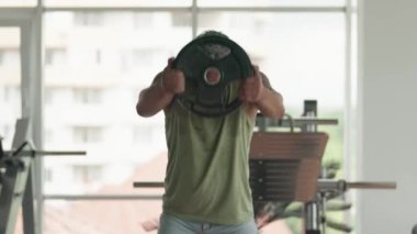 Modern bir spor salonunda ağırlık plakasıyla ağırlık kaldırma ve egzersiz yapmaya odaklanmış bir adam. Zindelik, güç ve kararlılık.