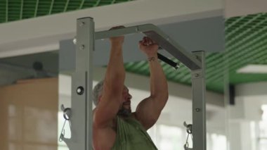 Spor salonunun barında barfiks çeken kaslı bir adam modern bir spor salonunda spor salonuna odaklanıyor..