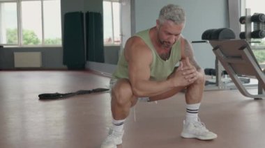 Adam antrenmana başlamadan önce spor salonunda ısınma hareketleri yapıyor. Sahnede hazırlık, spor ve sağlık vurgulanıyor..