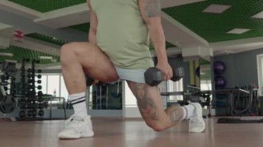 Modern spor salonunda dambılı ve dambılı dövmeli bir adam. Görüntü renklendirme uygunluğu, güç ve kararlılık.