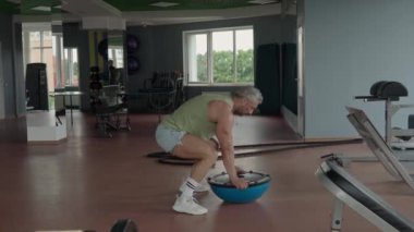 Geniş bir spor salonunda denge antrenörü kullanarak burpee egzersizi yapan bir adam. Yüksek yoğunluklu antrenman ve fiziksel koşullanma..