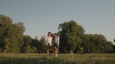 Romantik genç çift el ele tutuşup güzel güneşli bir parkta kameraya doğru yürüyorlar. Gülüyorlar ve mutlular. Yaz aşkı konsepti.