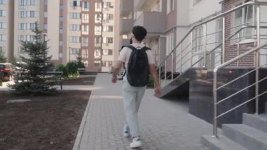 Gözlüklü ve siyah sırt çantalı genç bir adam apartmanın merdivenlerinden aşağı iniyor..