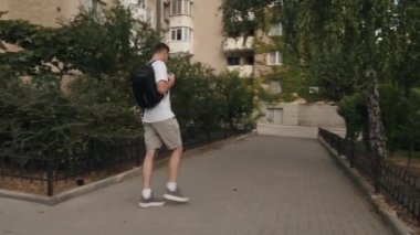 Sırt çantalı genç bir adam şehir caddesinde yürüyor. Yaz havasının, şehrin manzarasının ve seslerinin tadını çıkarıyor..