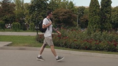 Sırt çantalı genç bir adam güneşli bir günde parkta yürür. Doğanın huzur ve sessizliğinin tadını çıkarıyor..