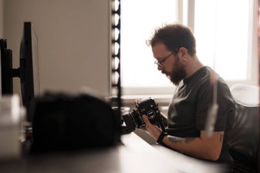 Odaklanmış erkek fotoğrafçı iyi aydınlatılmış bir odada klasik bir kamerayı kontrol ediyor. Fotoğraf konseptinde coşku ve uzmanlık.