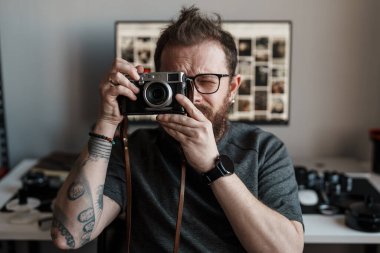 Arka planda fotoğrafçılık ekipmanları olan, stüdyo ortamında klasik fotoğraf makinesi kullanan odaklanmış bir fotoğrafçı..