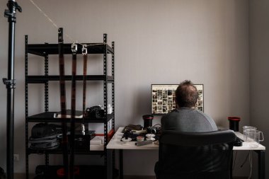 İyi düzenlenmiş bir ev stüdyosundaki fotoğraf makinesiyle fotoğrafları inceleyen bir fotoğrafçının arka görüntüsü..