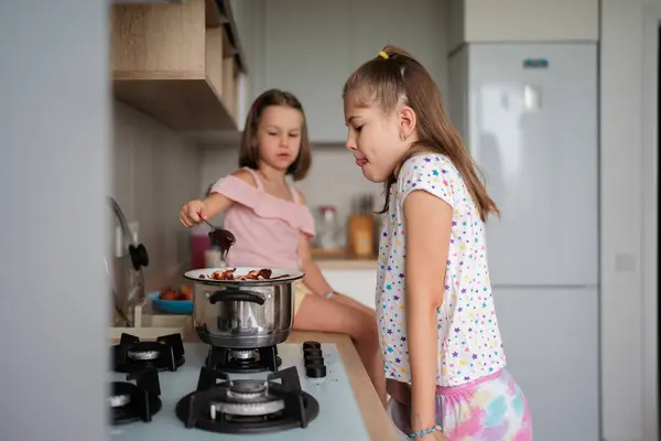 stock image Two young girls are cooking together in a modern kitchen, exploring the joy of culinary activities and friendship. They are actively engaged in preparing food on the stove.