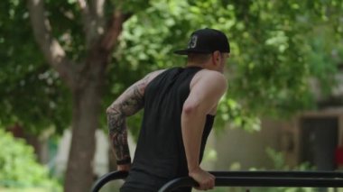 Açık havada egzersiz yapan genç bir atletik paralel barlarda yüzüyor. Odaklanmış ve sıkı çalışıyor..