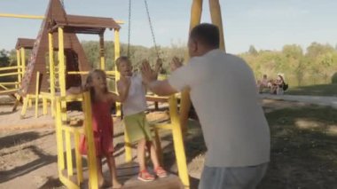 Mutlu bir aile parkta salıncakta sallanırken eğlenir. Baba, iki küçük çocuğuyla şakalaşarak çocukluk sevincinin ve aile bağının iç açıcı bir sahnesini yaratıyor..