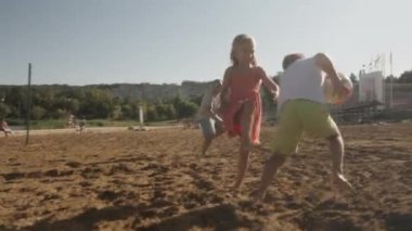 Mutlu bir aile kumsalda voleybol oynayarak güneşli bir günün tadını çıkarır. Küçük çocuklar koşuyor ve gülüyorlar babaları eğlenceli, gösterişli yaz neşesine ve aile bağlarına katılırken.