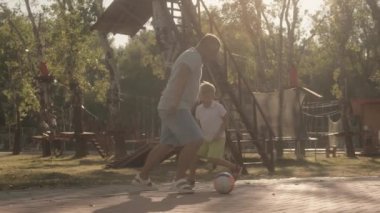 Bir baba ve oğlu parkta birlikte eğlenceli bir futbol oyunu oynuyor. Güneş parlıyor ve ikisi de harika vakit geçiriyor..
