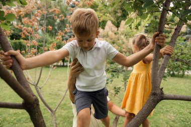 Güneşli bir günde bahçede oynayan ve ağaca tırmanan iki çocuk, açık hava eğlencesi ve macera sergiliyorlar..