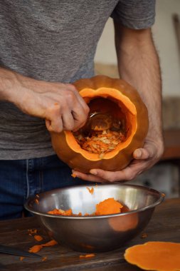 Close-up of a person carving a pumpkin, scooping out seeds and pulp into a metal bowl, preparing for Halloween. clipart