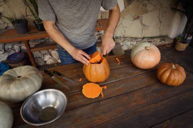 Bir insan kırsal bir masaya balkabağı oyup Cadılar Bayramı için hazırlıyor. Çeşitli balkabakları ve oyma aletleri rahat ve doğal bir ortamda sergilenir.