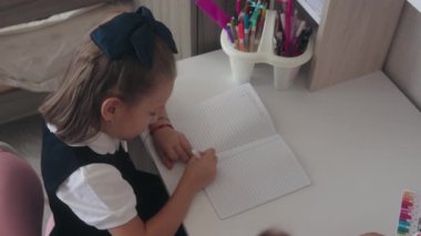 Genç liseli kız masadaki deftere yazıyor. Ödevlerini ya da derslerini yapıyor..