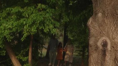 Mutlu bir aile parkta yürüyor. Ebeveynler kızlarının elini tutuyor..