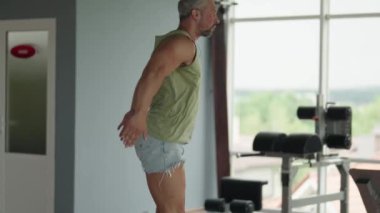 Geniş pencereli bir spor salonunda atlama egzersizi yapan adam güç, zindelik ve kararlılık gösteriyor..
