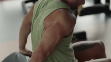 Bir adam trisepslerini spor salonunda makineye yaslanırken pompalıyor. Kol dayanıklılığına ve kas çalışmasına odaklan..