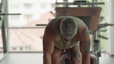 Spor salonunda dambıllarla egzersiz yapan dövmeli kaslı bir adam. Sağlıklı bir yaşam tarzına güç, uygunluk ve adanmışlık göstergesi.