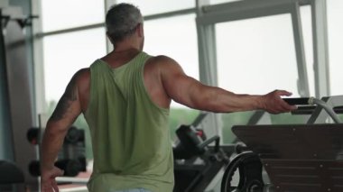 Modern bir spor salonunda antrenman yaptıktan sonra kolunu esneten atletik bir adam. Forma ve sağlığa bağlılığı gösterir.