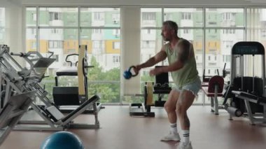 Modern bir spor salonunda bir çaydanlıkla çalışan bir adam. Spor malzemelerini kullanarak fitness ve dayanıklılık eğitimine odaklan.