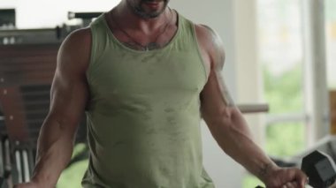 Spor salonunda dambılları kaldıran kaslı bir adamın yakın çekimi, egzersiz sırasında güç ve zindelik gösterisi..