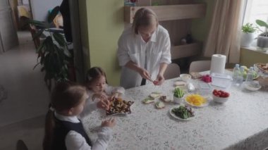 Anne kızları için sağlıklı okul yemeği hazırlıyor. Aile mutfakta, okul için yemek hazırlıyor. Kızlar okul üniforması giyiyor..