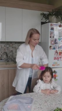 Anne okuldan önce kızının saçını tarar. Sabahları hazırlanmak, çocuk bakımı, annelik ve aile hazırlığı..