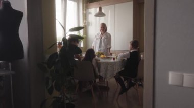 Bir anne, okul öncesi çocuklarına talimat ya da cesaret verirken bir aile mutfak masasında oturur. Okul, kahvaltı, aile, destek, çocuklar, çocuklar için hazırlanıyorum..