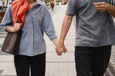 Şehir caddesinde yürürken el ele tutuşan bir çift. Gündelik yaz kıyafetleri giyiyorlar, aşkı ve birlikteliği somutlaştırıyorlar. Sahne bir şehir romantizmi ve bağlantı anını yakalıyor.